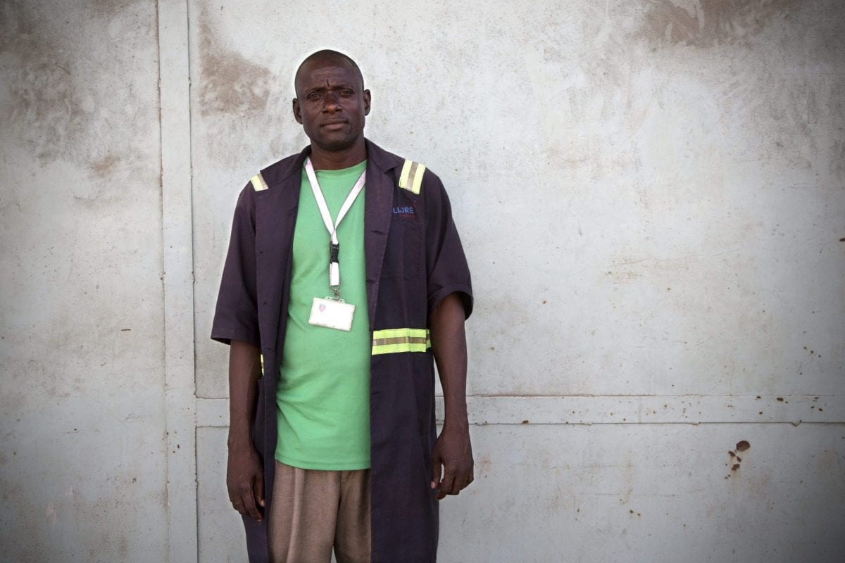 Charles Ebuya er 41 år gammel og har været bærer i 12 år. Han er “regular” men har aldrig set en kontrakt. Løn: 500 shilling (ca. 32 kr.) for en vagt på 8 timer, der ifølge flere arbejdere uden for varehuset ofte bliver til 12 – uden ekstra betaling.